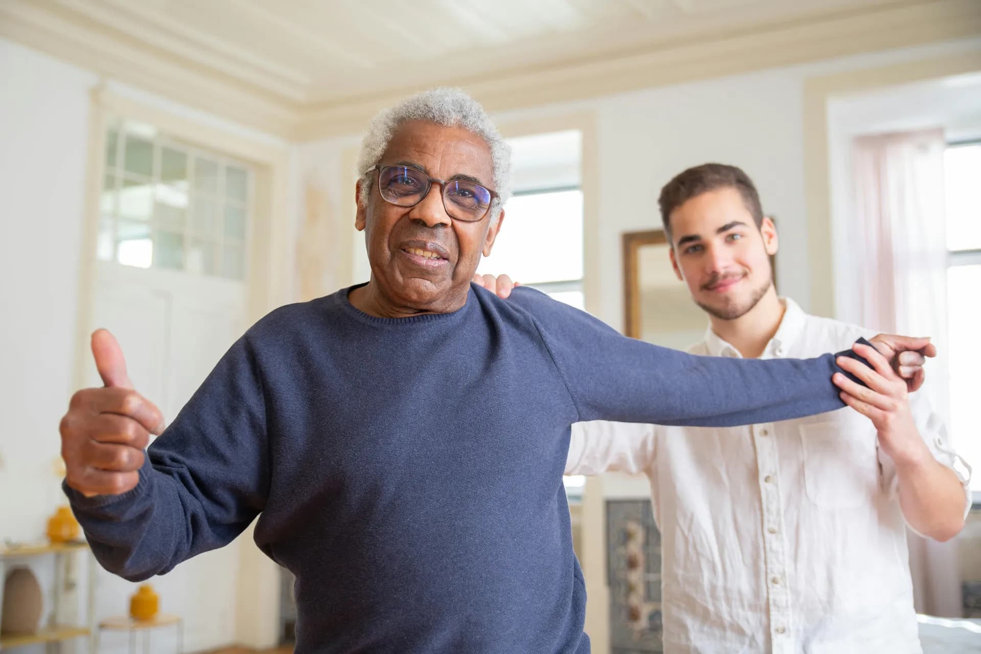An elderly man with his caregiver, smiling with thumbs up